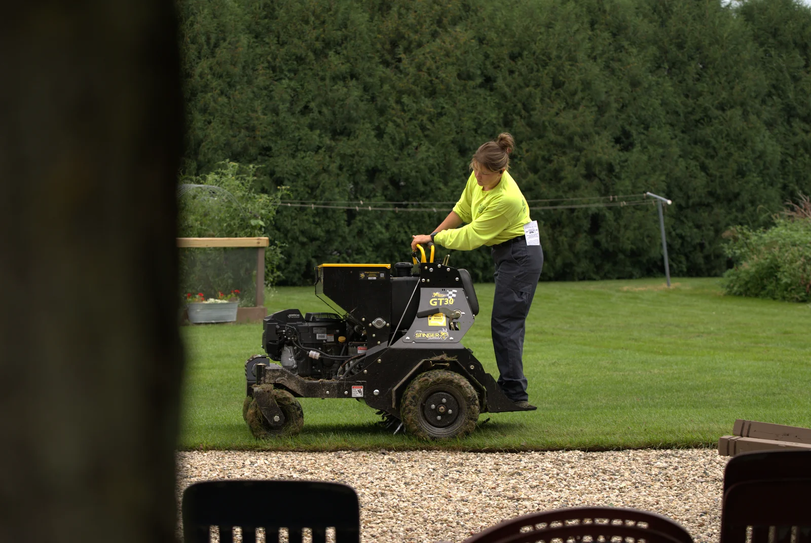 Green Acres crew member in high-visibility shirt performing lawn aeration service on residential property