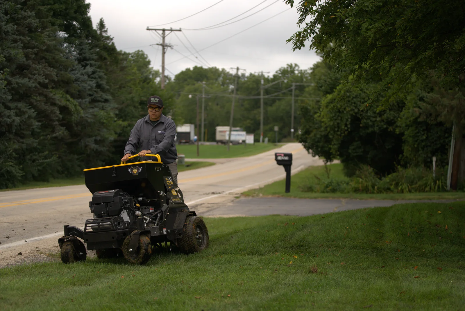 Green Acres crew member performing lawn aeration service with stand-on aerator on residential property
