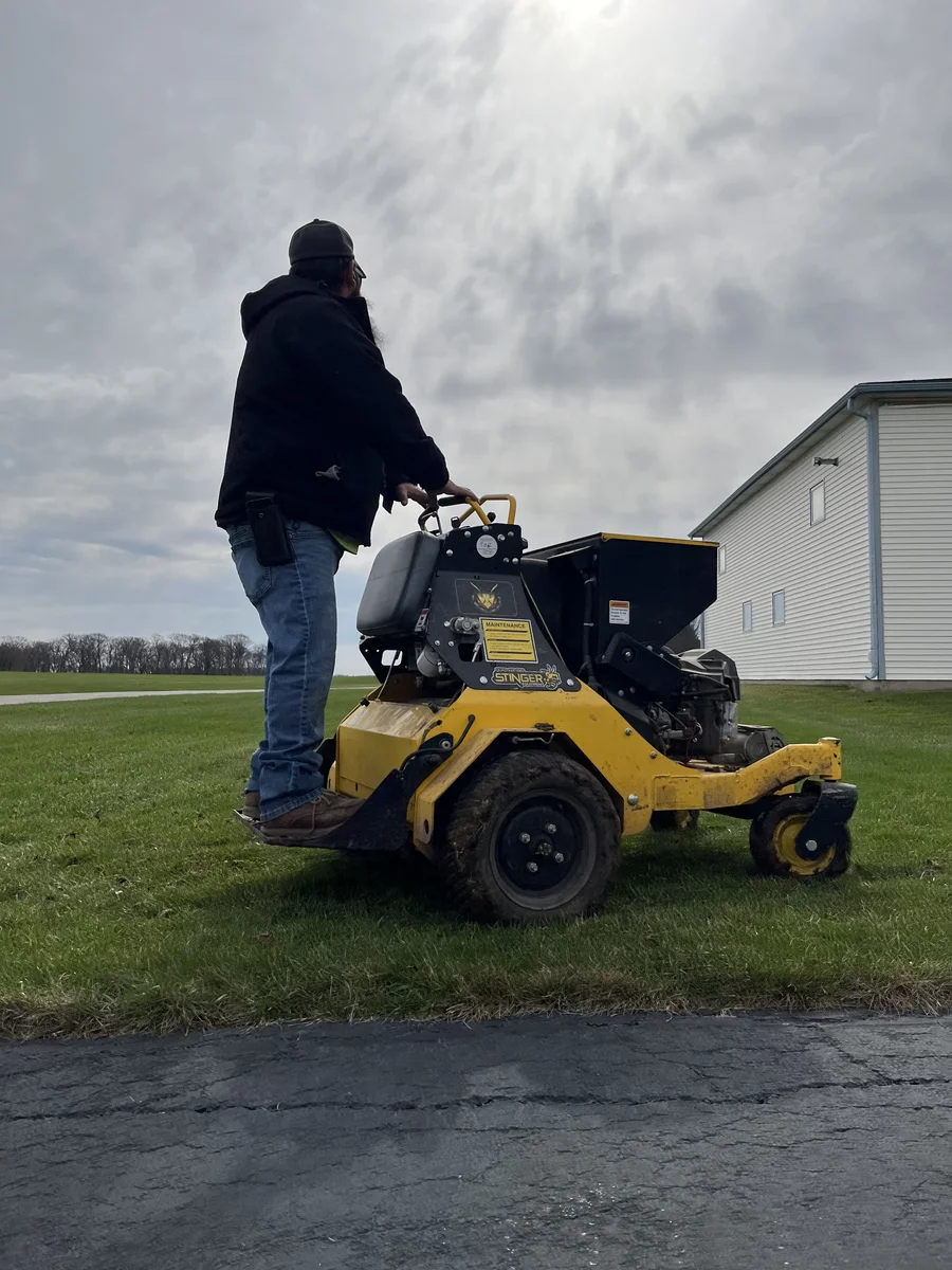 Green Acres crew member performing lawn aeration service with yellow stand-on aerator machine on residential property