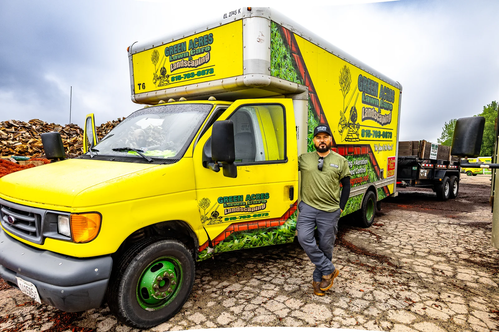 Green Acres Landscaping crew member standing beside bright yellow branded company truck with service graphics