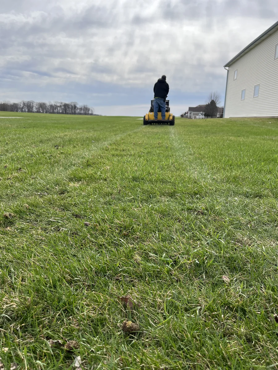 Green Acres crew member operating yellow stand-on mower on large residential lawn