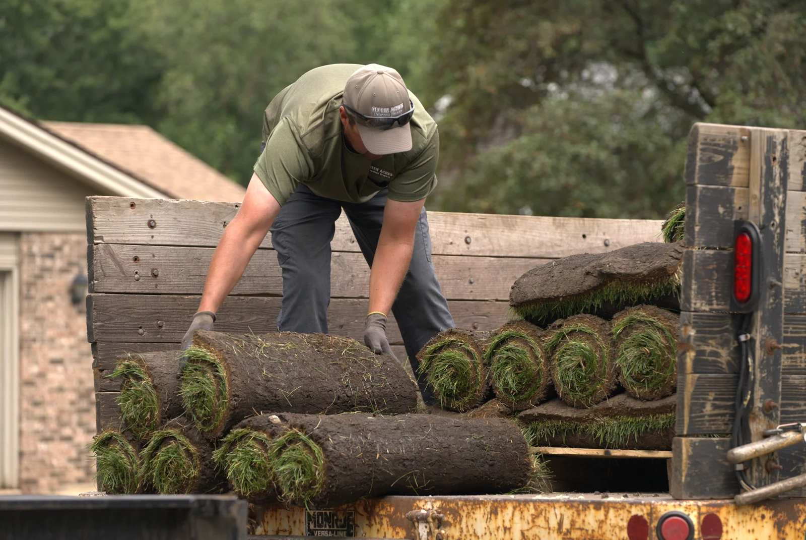 Green Acres crew member unloading fresh sod rolls from trailer for residential lawn installation
